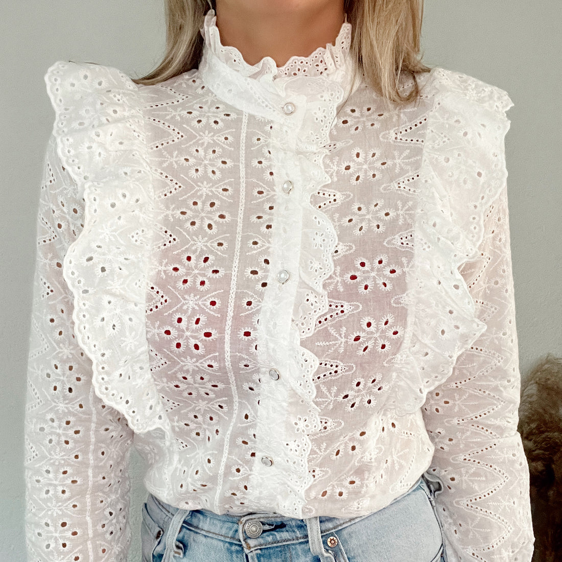 Witte broderie blouse met ruffle detail en parelmoer knoopjes. De blouse is van 100% katoen en valt normaal op maat. Witte broderie blouse met ruches en parelmoer knopen katoen.