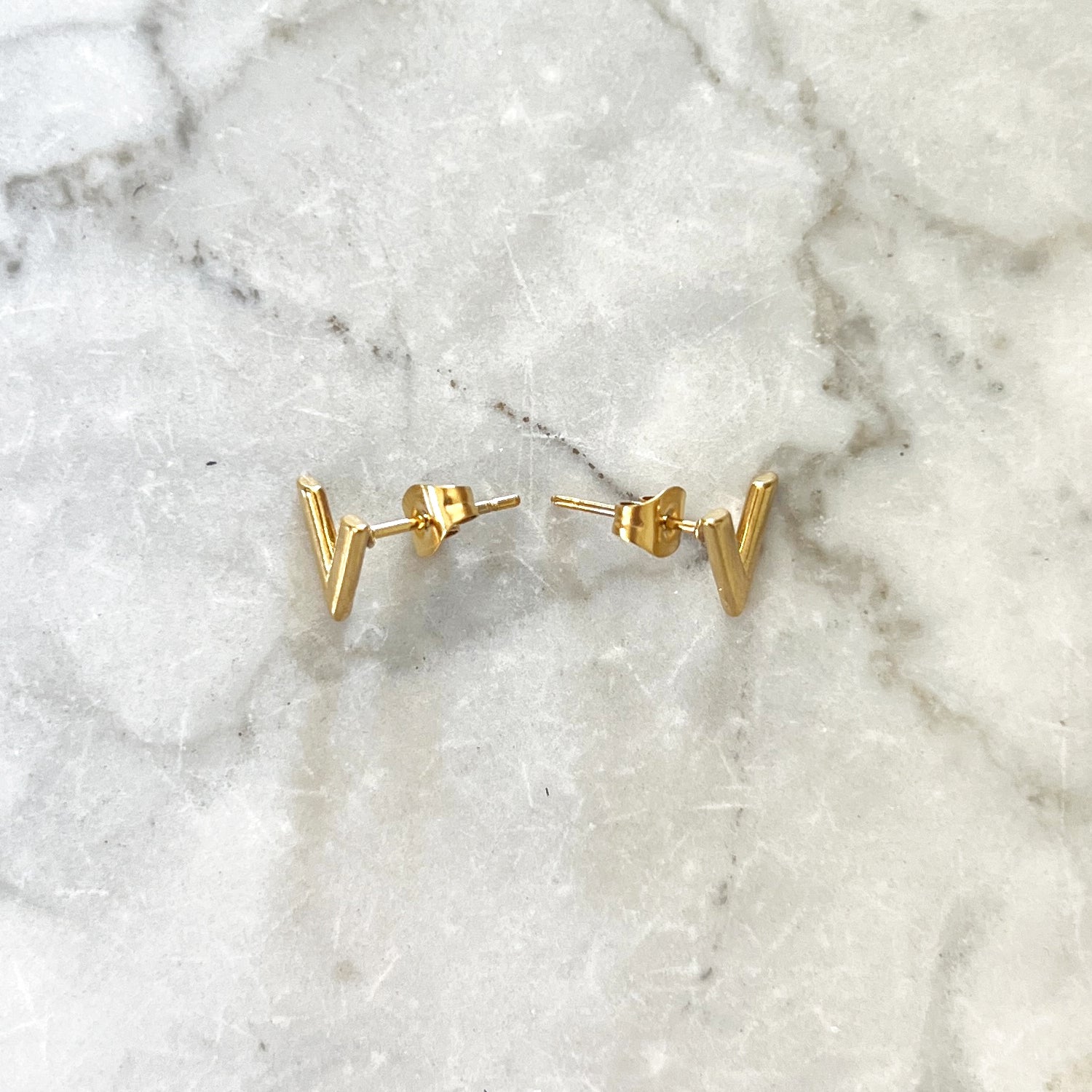 Gouden oorbel studs in de vorm van een V. De oorbellen zijn van roestvrij staal met een gold plated laagje en waterproof. V studs gold 10 mm.