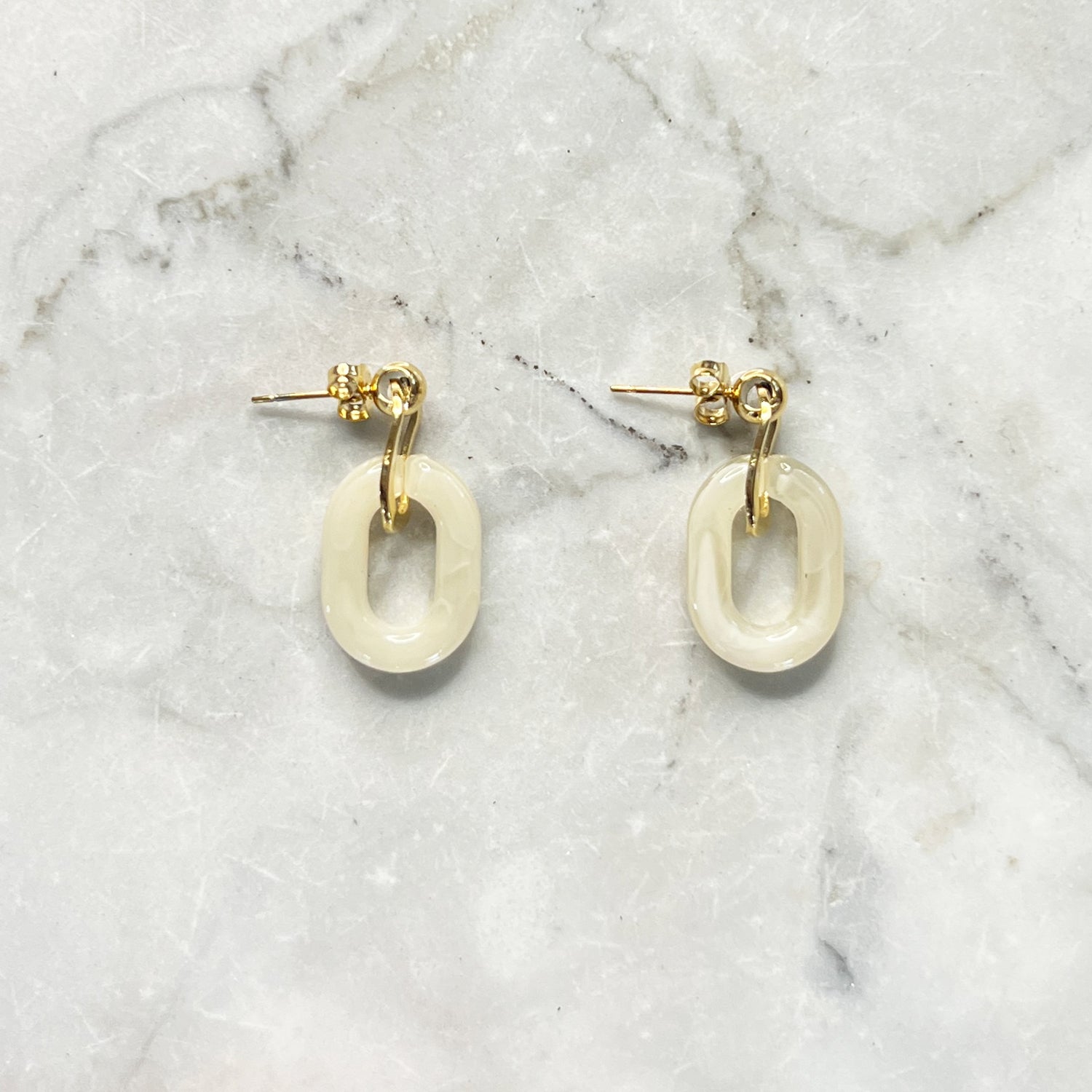 Gouden oorbellen met een beige ovale hanger er aan. De oorbellen zijn van gold plated stainless steel materiaal en zijn waterproof.   Afmetingen: 3 cm 