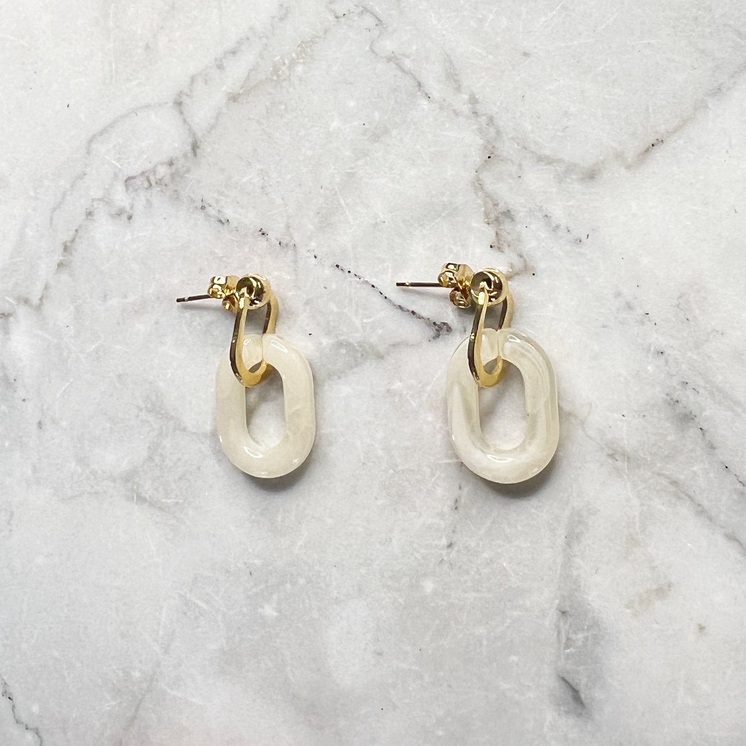 Gouden oorbellen met een beige ovale hanger er aan. De oorbellen zijn van gold plated stainless steel materiaal en zijn waterproof.   Afmetingen: 3 cm 